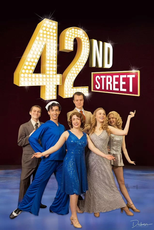 Six young people pose in gold and blue costumes against a black backdrop and a lit up Forty Second Street sign.